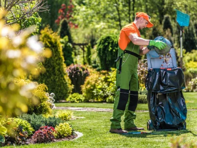 gardener working in the green garden and cleaning it from leaves and grass